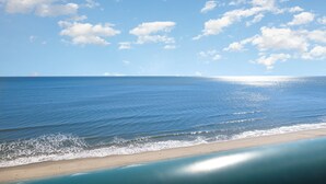 A beach with clear blue water and a sandy shore under a bright sky with scattered clouds. - Spectacular 3 BR 2 BA Ocean Front Condo (Myrtle Beach)