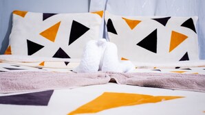 Un letto rifatto con cura, con una coperta a motivi geometrici, due cuscini con un design simile e un paio di asciugamani bianchi piegati ai piedi del letto.