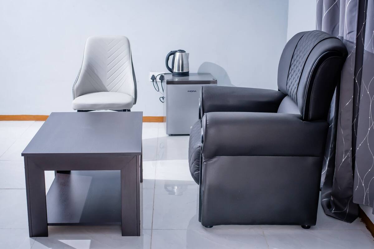 A modern living area with a sofa, a chair, a coffee table, and a small side table with a kettle.