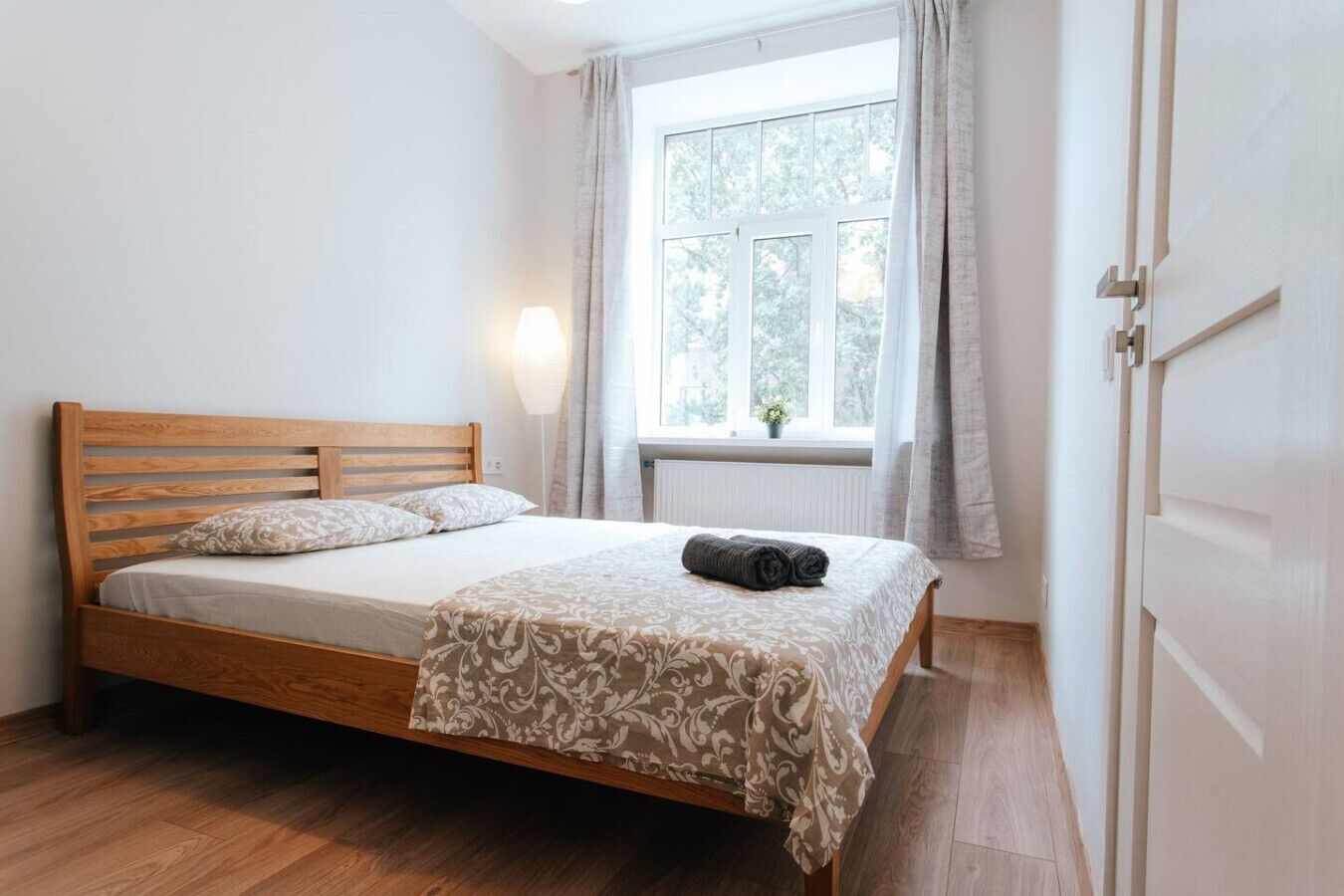 Ein ordentlich bezogenes Bett mit einem Holzkopfstück, einer gemusterten Tagesdecke und einem zusammengerollten Handtuch daneben.