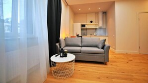 Un salon moderne avec un canapé gris, une table basse ronde et un coin cuisine à l’arrière-plan.