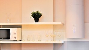 Une cuisine équipée d’un four à micro-ondes, d’une plante en pot et de verres à vin placés sur une étagère.