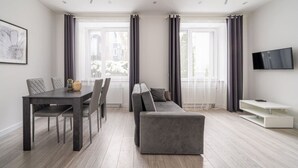 Un salon moderne comprenant un coin repas, un canapé gris et un téléviseur à écran plat fixé au mur.