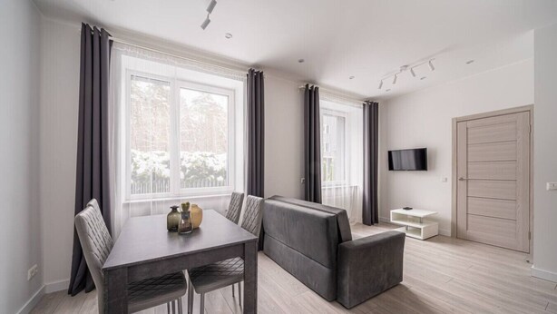 Un salon moderne avec une table à manger, un canapé gris et un téléviseur fixé au mur.
