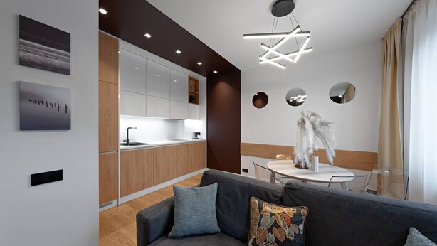 Una sala de estar moderna con un sofá gris, una mesa de comedor y una cocina con armarios blancos y encimera de madera.