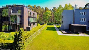 Un complejo residencial moderno con varias edificaciones, un césped bien cuidado y un fondo boscoso.