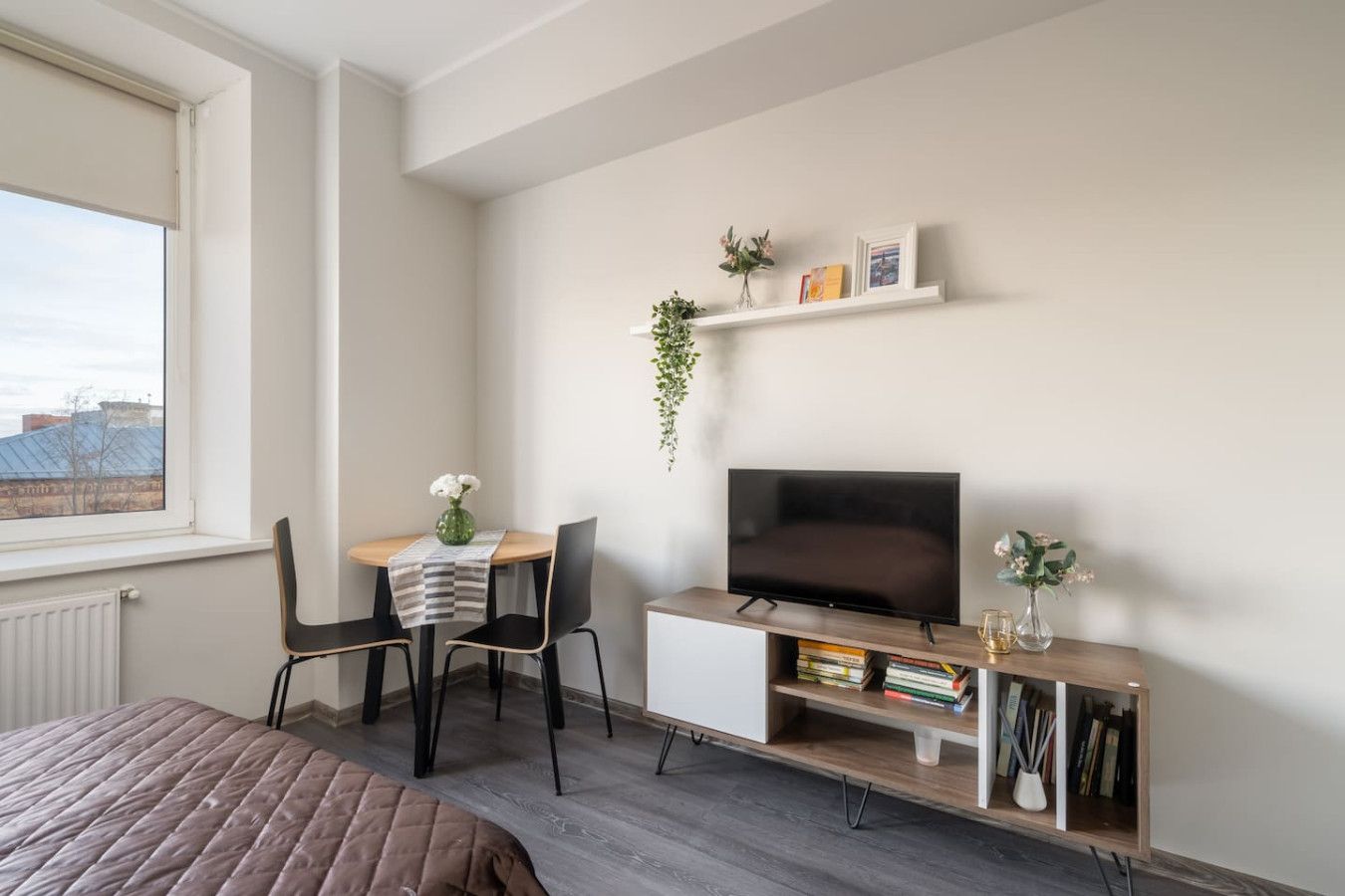 Un dormitorio moderno con cama, televisor, una pequeña mesa con sillas y una estantería.