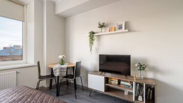Un dormitorio moderno con cama, televisor, una pequeña mesa con sillas y una estantería.