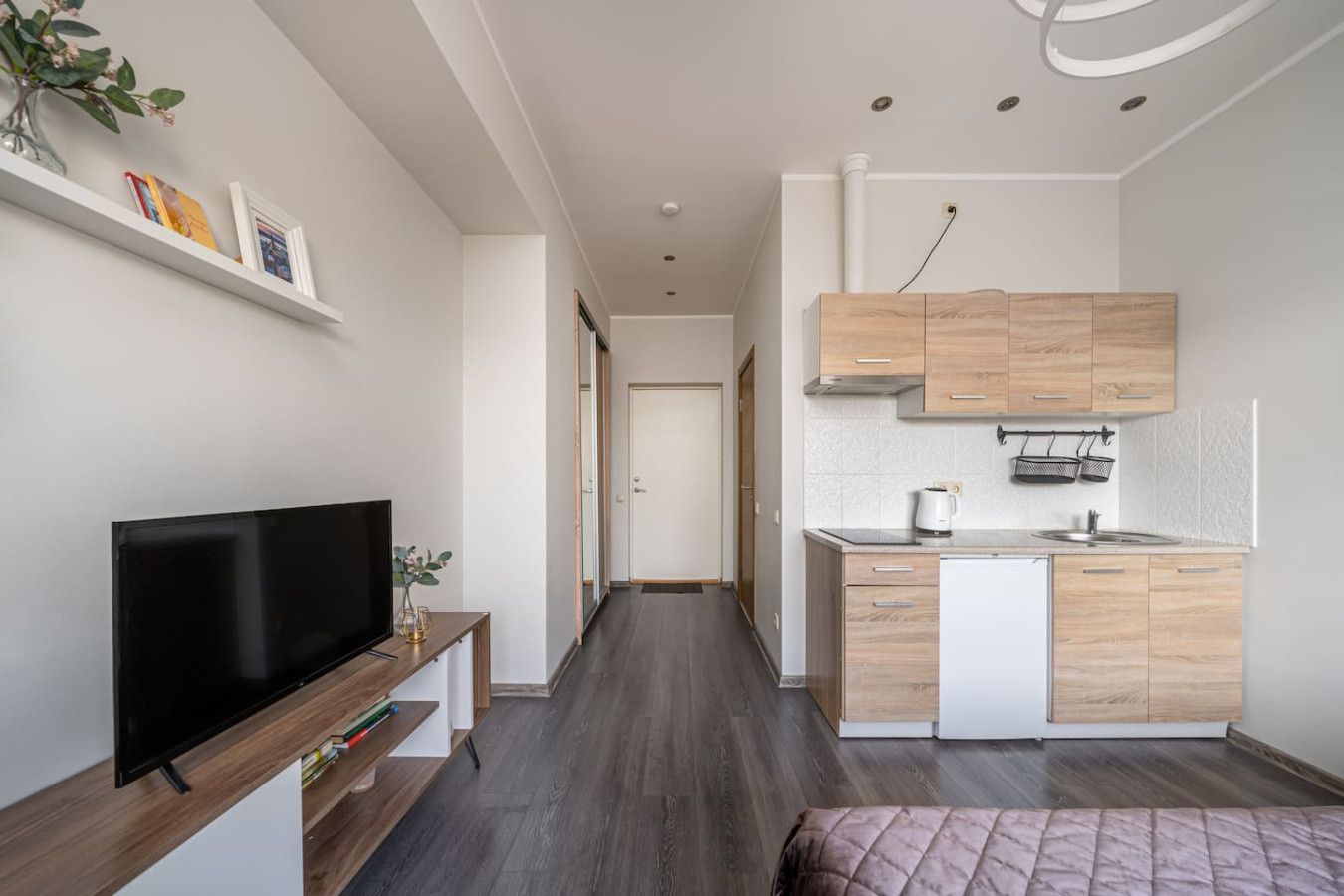 Un espacio habitable pequeño con kitchenette, televisor de pantalla plana y cama.