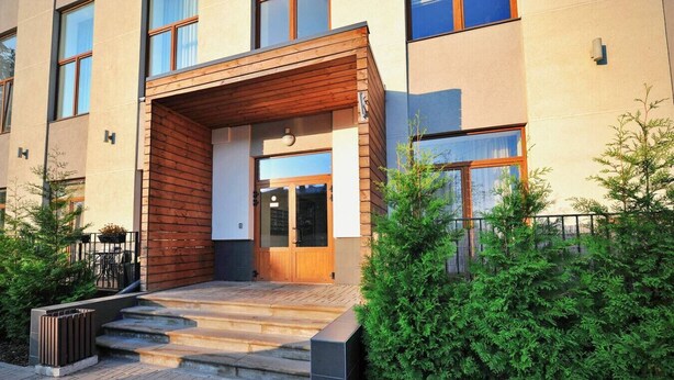 Een modern gebouw met een houten entree, trappen die naar een glazen deur leiden, en een klein terras.