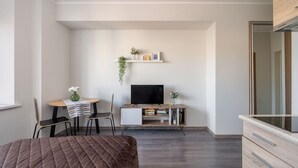 Een knus slaapkamer met een bed, een bureau met stoel, een televisie en een plank met boeken en een plant.