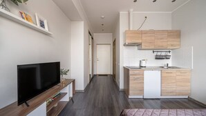 Een modern appartement met een televisie, houten meubels, een kitchenette en een gang.