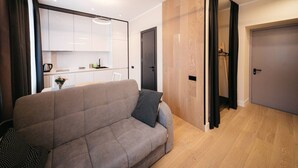 Un soggiorno moderno con un divano grigio, una parete divisoria in legno e una cucina sullo sfondo.