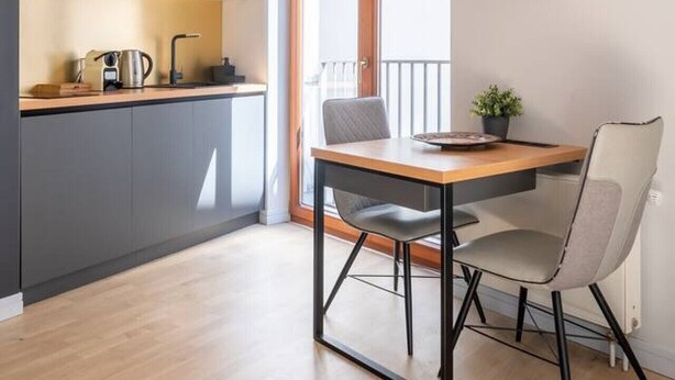 Une cuisine moderne avec des meubles en bois, un plan de travail noir et un coin repas comprenant une table et des chaises.
