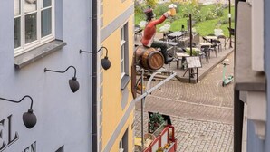 Eine enge Straße mit Kopfsteinpflaster, ein Gebäude mit der Aufschrift "EL KITCHEN" und eine Statue eines Mannes, der aus einem Fass etwas ausgießt.