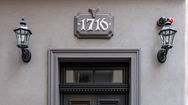 A black double door with a number plaque '1716' above it, flanked by two wall-mounted lanterns.