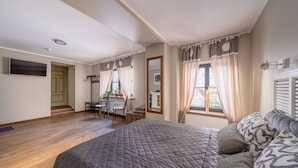 A bedroom with a large bed, a desk with a chair, a window with curtains, and a radiator.