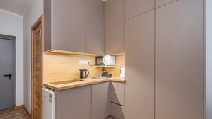 A compact kitchen with a wooden countertop, a built-in microwave, a kettle, and a small refrigerator. - Dzintaru studio apartment (Jūrmala)