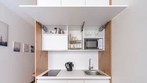 A compact kitchen with white cabinets, a microwave, a kettle, and a sink.