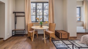 Una habitación con una mesa redonda de madera, dos sillas de mimbre, un pequeño banco y una ventana que ofrece vistas a un edificio con andamios.