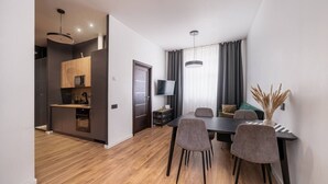 Ein modernes Wohnzimmer mit Essbereich, ausgestattet mit einem dunklen Esstisch aus Holz, grauen Polsterstühlen und einem an der Wand montierten Flachbildfernseher.