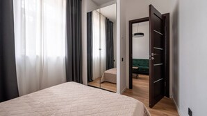 Ein Schlafzimmer mit einem Bett, einem Spiegel und Blick in einen anderen Raum mit einem grünen Sofa.