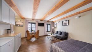 A compact room with a bed, a sofa, a dining table with chairs, and a kitchenette.