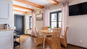 A cozy room with a dining table, wicker chairs, a kitchen area with a kettle, and a TV mounted on the wall.