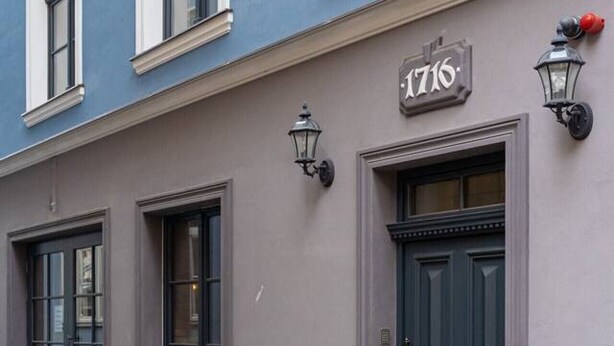 A building with a blue facade, numbered 1716, featuring dark wooden doors and windows with white frames.