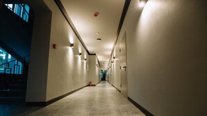 Un largo y estrecho pasillo de hotel con pisos y paredes de cerámica, equipado con letreros de salida de emergencia y un extintor.