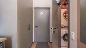 Un pasillo estrecho que conduce a una puerta con un cartel de prohibido fumar, una lavadora y un estante pequeño con toallas.