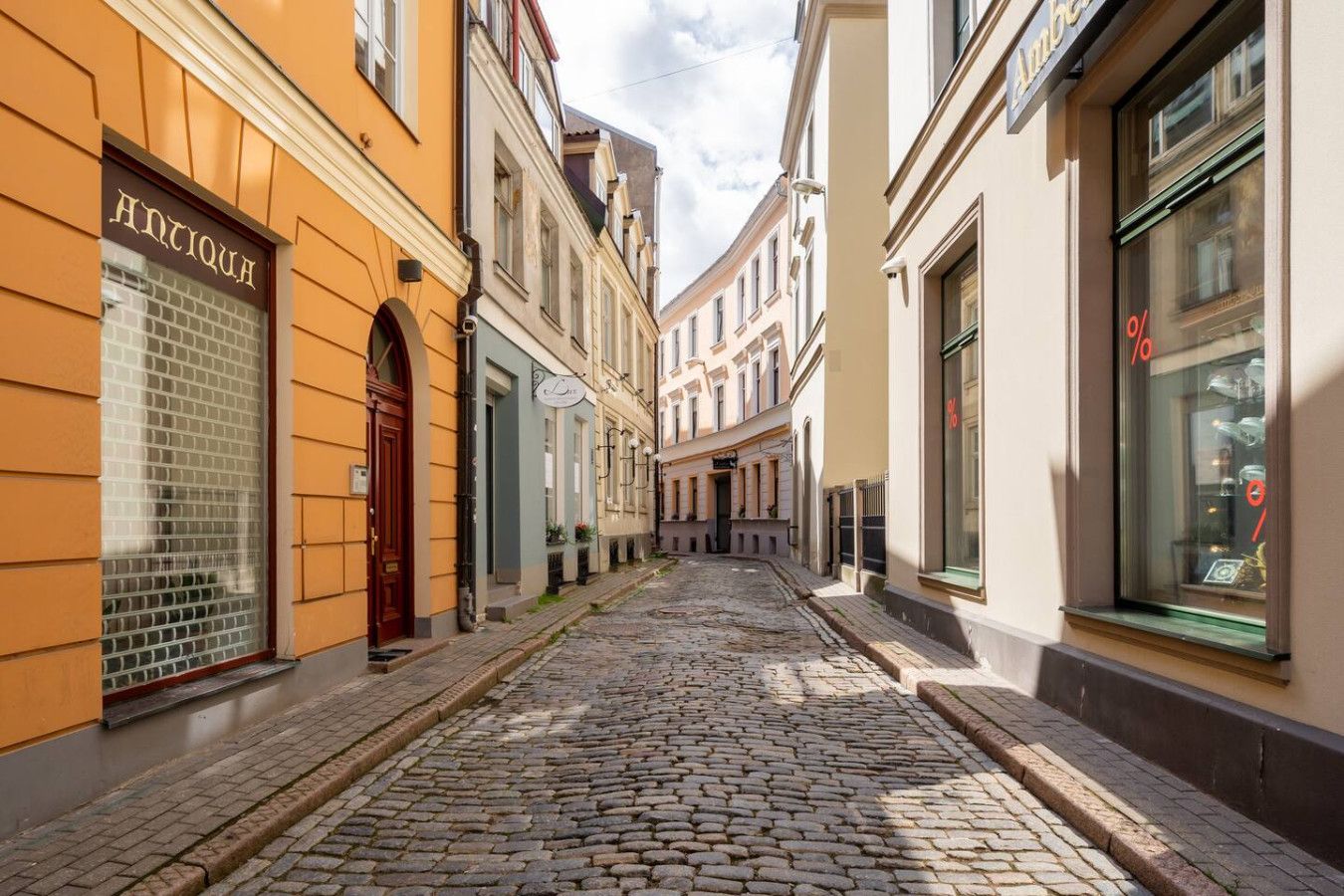 A cobblestone street lined with historic buildings, a shop with a visible sign, and a window with a percentage sign.