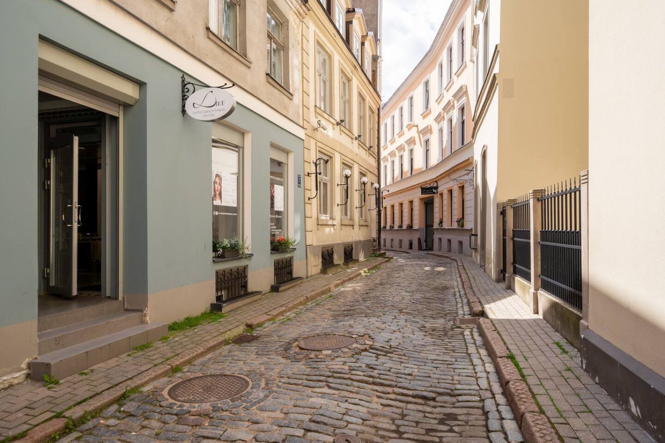 A narrow cobblestone street flanked by historic buildings with visible storefronts and a manhole cover.