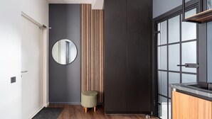 A modern kitchen with dark cabinetry, a round mirror, and a wooden accent wall. - Top Location – Spacious Bath – New and Cozy (Rīga)