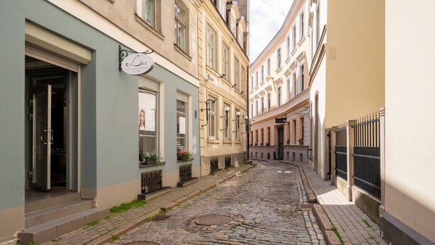 A narrow cobblestone street flanked by historic buildings with a sign indicating a spa. - Top Location – Spacious Bath – New and Cozy (Rīga)