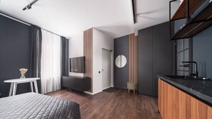 A modern hotel room with a bed, a small table with a vase, a TV mounted on the wall, a round mirror, and a wooden cabinet with a sink. - Top Location – Spacious Bath – New and Cozy (Rīga)