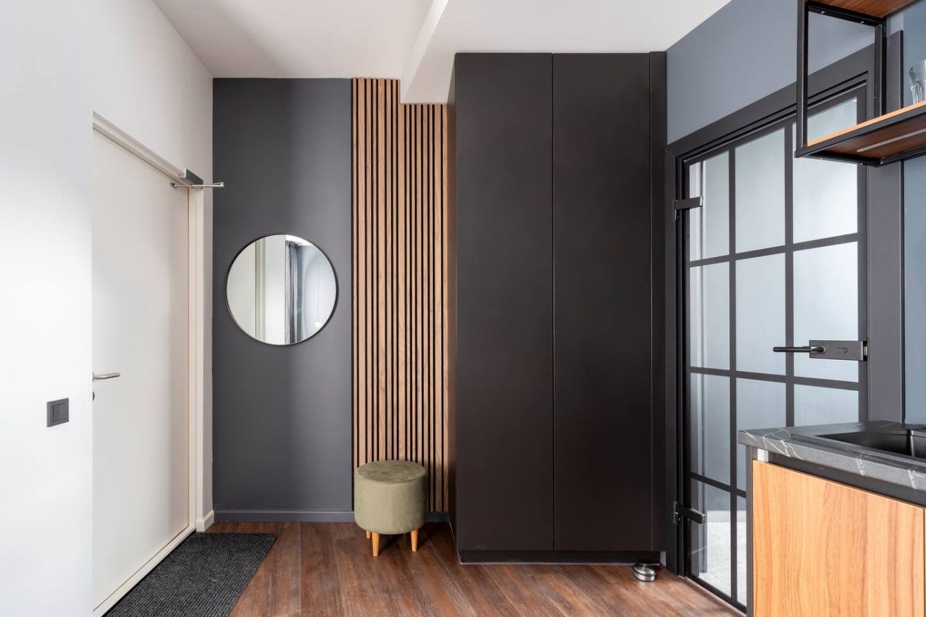 Una cocina moderna con armarios oscuros, un espejo redondo y un panel de pared de listones de madera.