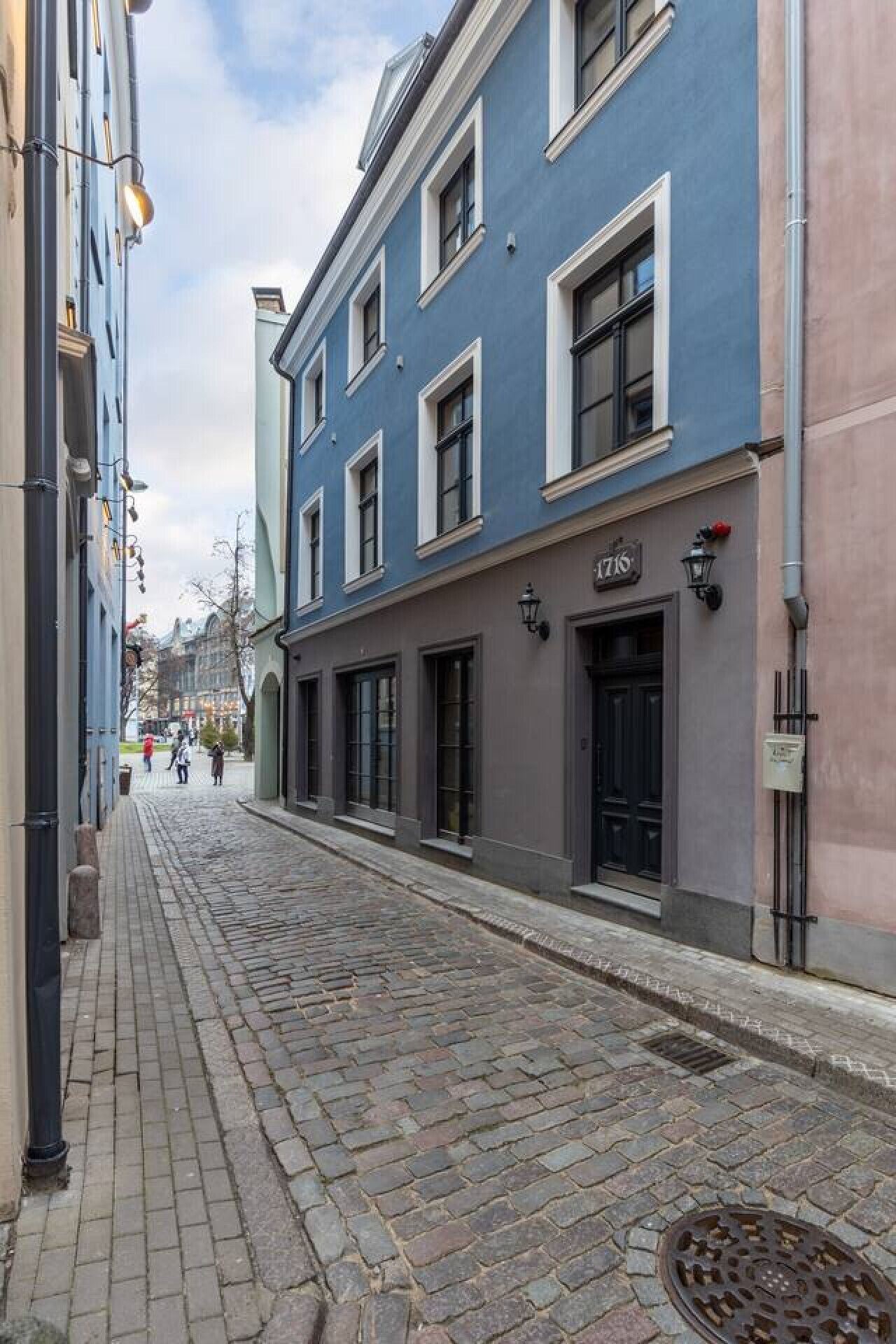 A cobblestone street lined with buildings, including a blue building with a black door and a sign that reads "ZATIS".
