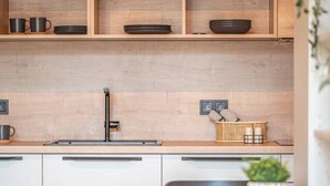 Una cocina moderna con armarios de madera, un grifo negro y un comedor con mesa y sillas de madera, todo en color negro.