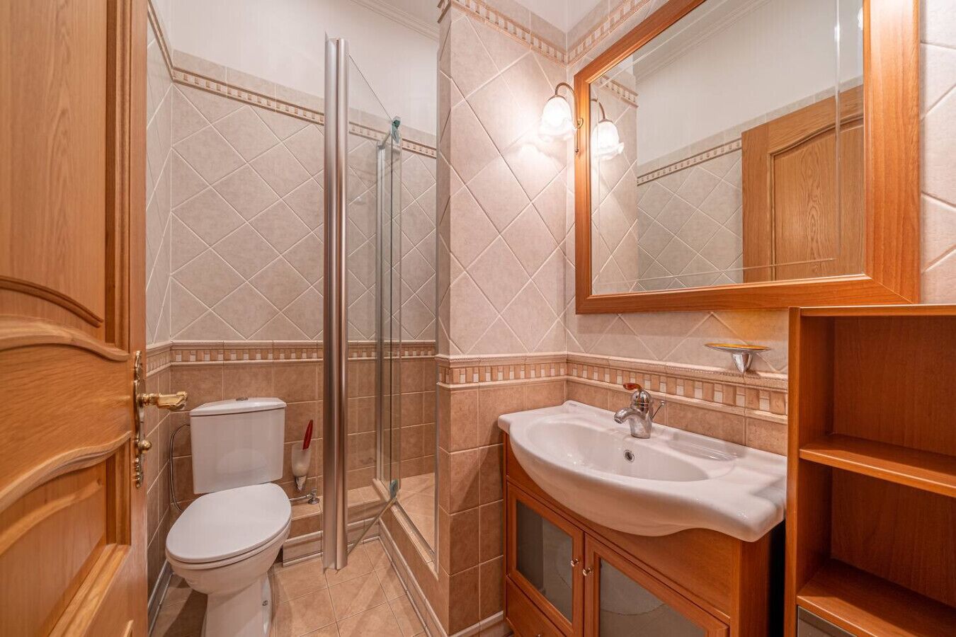 A bathroom with a glass shower enclosure, a white toilet, a sink with a mirror, and wooden cabinetry.