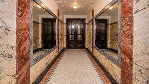Un pasillo de mármol con una puerta central, flanqueado por espejos e iluminación empotrada.