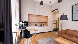 Una cocina moderna con armarios blancos, encimera de madera y una silla negra. Hay un sofá marrón y una lámpara en la sala de estar.