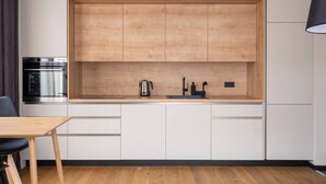 Una cocina moderna con armarios de madera, horno de acero inoxidable, hervidor y pileta.