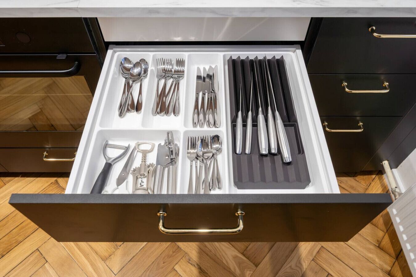 A drawer with neatly organized kitchen utensils including spoons, forks, knives, and a grater.