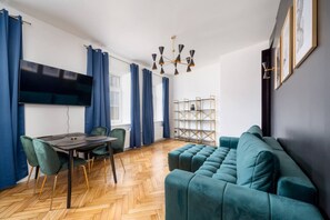 Una sala de estar moderna con un sofá, una mesa de comedor con sillas, un televisor y una araña.