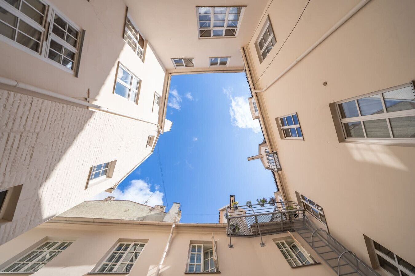 A narrow street with buildings on both sides, featuring multiple windows and a clear blue sky.