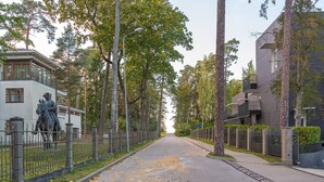 A street lined with trees and a statue, with modern buildings on either side. - Trendy beach-front 1-bedroom apartment in Dzintari (Jūrmala)