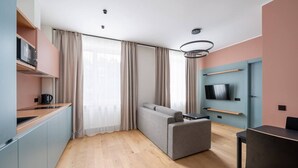 A compact living space with a kitchenette, a sofa, a TV mounted on the wall, and a dining table. - Trendy beach-front 1-bedroom apartment in Dzintari (Jūrmala)