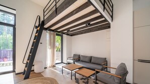 Uma sala de estar moderna com escada, sofá, mesa de centro e vista através de uma porta de vidro.