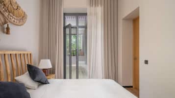 A bedroom with a bed, a wooden headboard, a nightstand with a lamp, and a view through a glass door to an outdoor area.